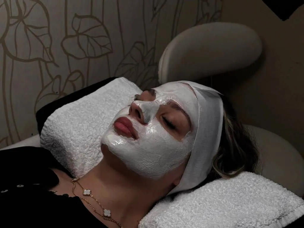 Kundin mit pflegender Gesichtsmaske und Stirnband während einer entspannenden Facial-Behandlung im Studio.